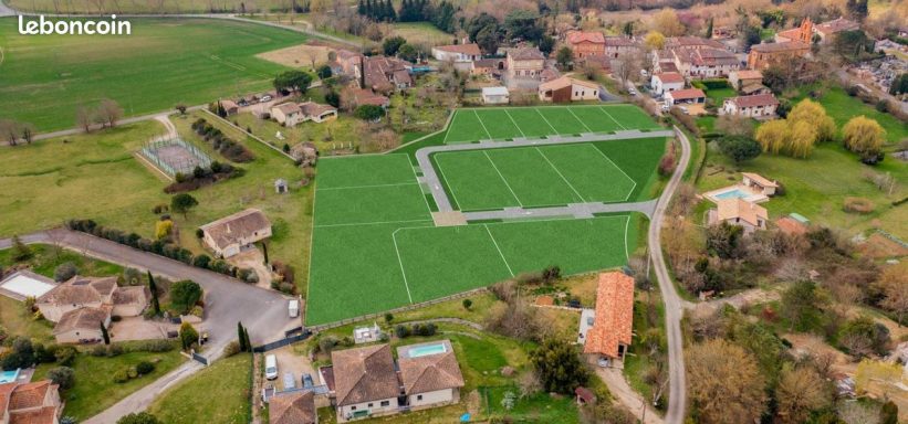 Vue aérienne d'un terrain de sport entouré de bâtiments et de verdure.